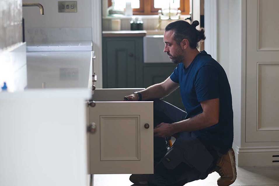 a plumber fixing a leak under the cupboard