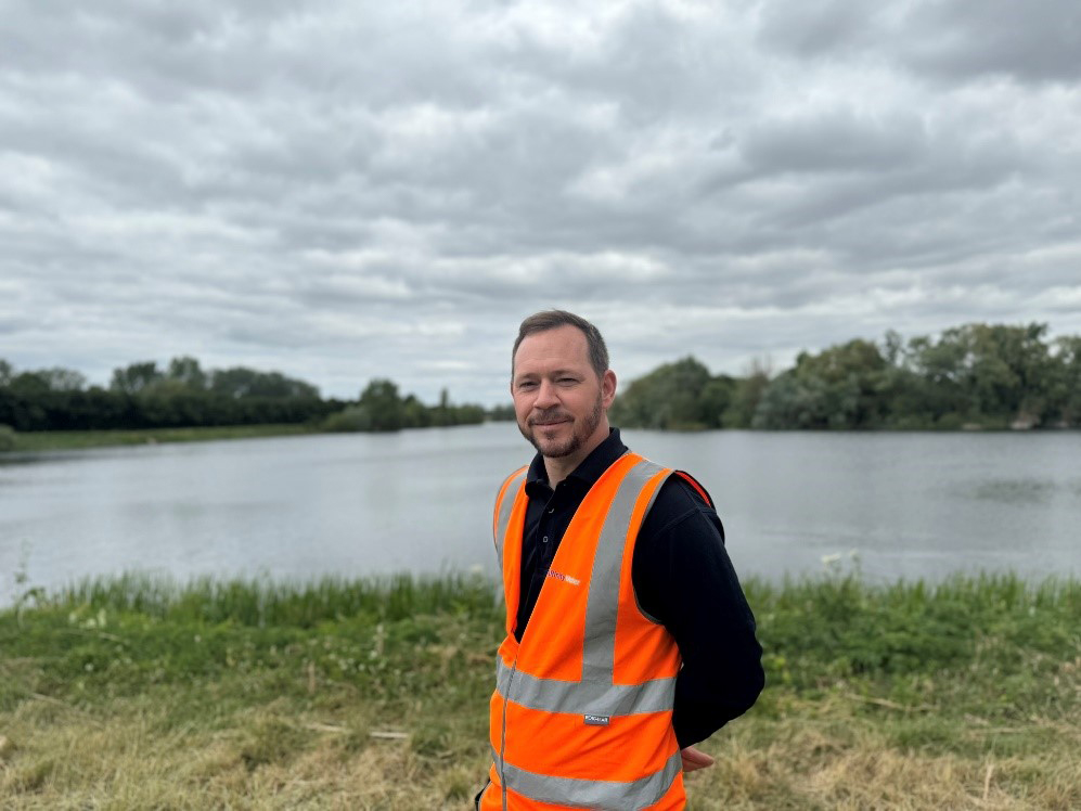 A person in an orange vest standing in front of a body of water
