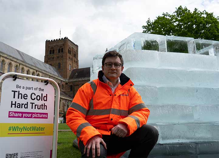 Jake Rigg standing outside St.Albans Cathedral besides the #WhyNotWater Cold Hard Truth art installation.
