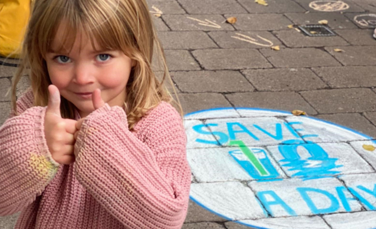 Child doing a thumbs up with the save 10 a day logo in chalk, on the pavement
